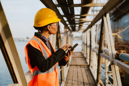 Black woman wearing helmet and vest working with tablet computer in portの写真素材