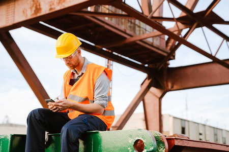 White ginger man wearing helmet and vest using cellphone working in portの写真素材