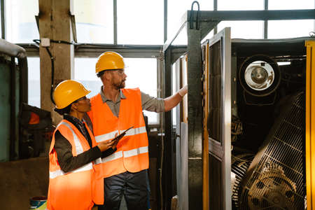 Multiracial man and woman in protective clothing working with equipment at factoryの写真素材