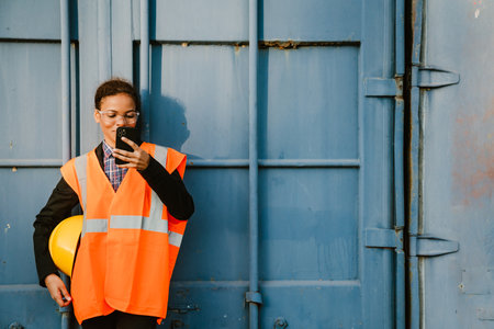Black woman wearing vest using mobile phone while working outdoors