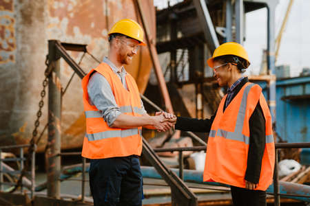 Multiracial man and woman wearing helmets handshaking while working at portの写真素材