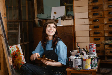Young woman wearing overall painting on canvas while sitting on floor at her studioの写真素材