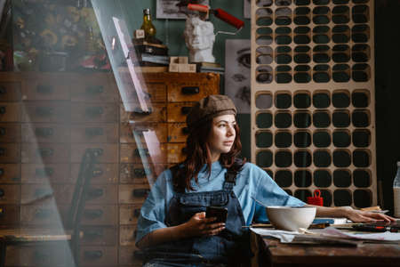 Young woman wearing overall using mobile phone while working in her studio