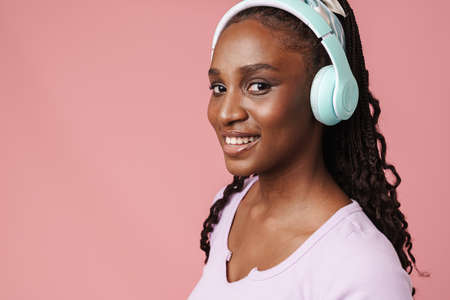 Black young woman smiling while listening music with headphones isolated over pink wallの写真素材