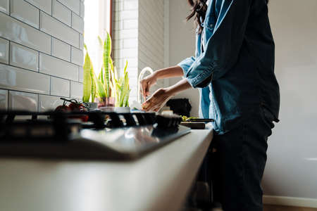 Black young woman wearing denim clothes cooking in kitchen at homeの写真素材