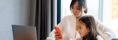 Asian woman and her daughter using laptop and cellphone at homeの写真素材