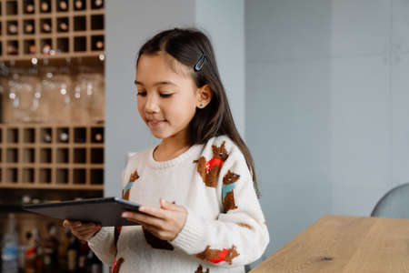 Asian girl using tablet computer while sitting at table at homeの写真素材