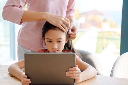 Asian woman and her daughter using tablet computer while spending time together at home
