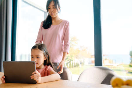 Asian woman and her daughter using tablet computer while spending time together at homeの写真素材