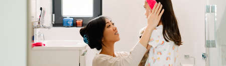 Asian mother wearing headband on her daughter in bathroom at homeの写真素材