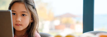 Asian girl using tablet computer while sitting at table at homeの写真素材