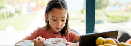 Asian girl using tablet computer while having breakfast at home