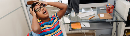 Black boy with headache holding his head and sitting on chair at homeの写真素材
