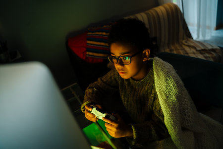 Black boy in eyeglasses using joystick while playing online game at home