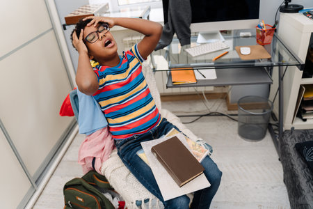 Black boy with headache doing homework while sitting on chair at home