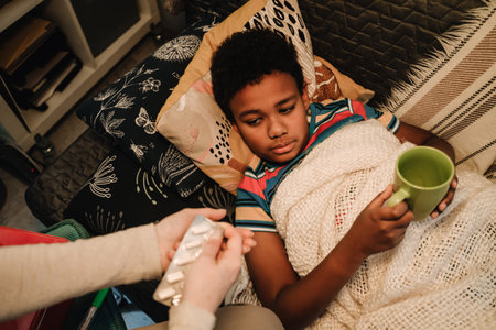 Mother giving medicine to sick son while taking care of him at homeの写真素材