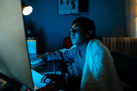 Black boy in eyeglasses working with computer while sitting at table at home