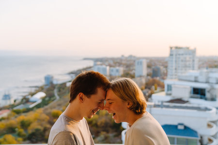 European gay couple laughing while standing head to head on balcony at home