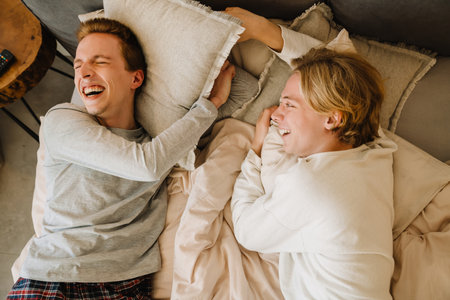 European gay couple laughing and making fun while lying on bed at home