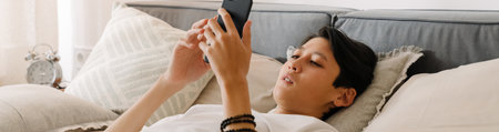 Asian boy using mobile phone while resting on bed at home