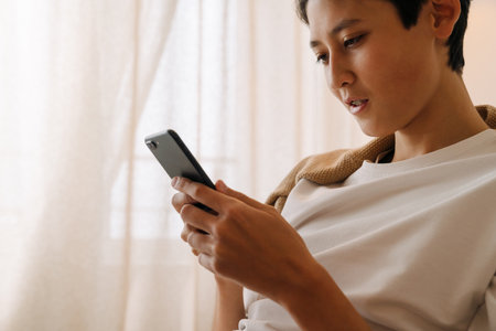 Asian boy with brace using mobile phone while resting at homeの写真素材