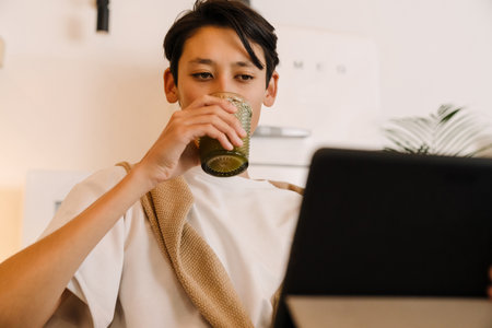 Asian boy using tablet computer while drinking kitchen in kitchen at homeの写真素材