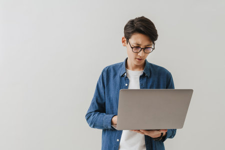 Asian brunette boy wearing eyeglasses working with laptop isolated over white backgroundの写真素材