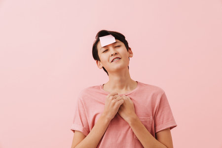 Asian boy smiling while posing with sticker on forehead isolated over pink backgroundの写真素材