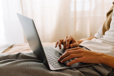 Asian boy working with laptop while resting on bed at home