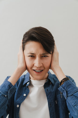 Asian boy wearing shirt covering his ears while posing on camera isolated over white background