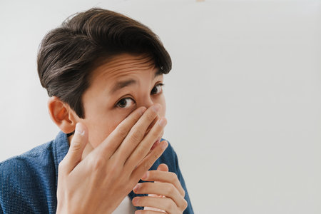 Asian boy wearing shirt touching her face and looking at camera isolated over white backgroundの写真素材