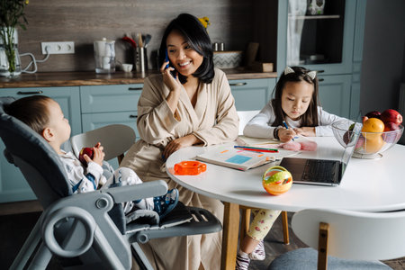Happy mother talking on cellphone while spending time with her children at homeの写真素材