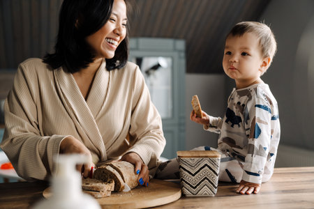Happy mother making fun with her son while cutting bread at homeの写真素材