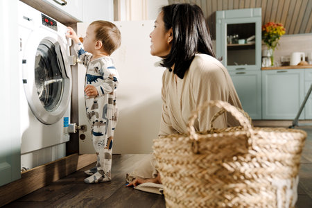 Happy mother smiling while doing housework with her son with her son at homeの写真素材