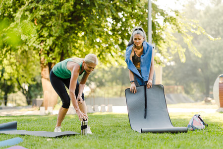 Multiracial women unrolling their mats during yoga practice in summer park