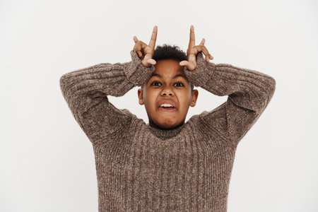 Black preteen boy making horn gesture and grimacing at camera isolated over white backgroundの写真素材