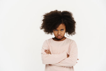 Black preteen girl with curly hair frowning and looking at camera isolated over white backgroundの写真素材