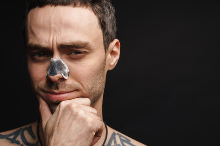 Mid aged white shirtless man using cleansing strip for nose over black wall backgroundの写真素材