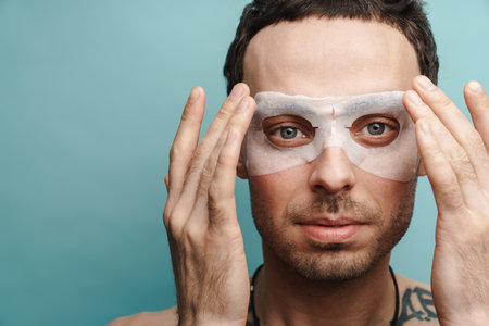 Close up of a shirtless mid aged brunette man wearing cosmetic eye mask over yellow wall backgroundの写真素材
