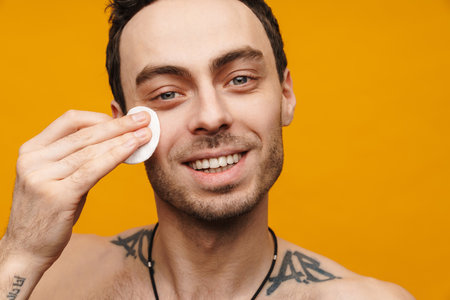 Close up portrait of a smiling shirtless mid aged man using cotton on his face over yellow wallの写真素材