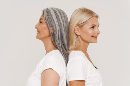 Mature multiracial women with gray hair wearing t-shirts posing at camera isolated over white backgroundの写真素材