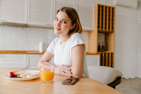 Smiling young woman having healthy breakfast sitting in the kitchen at homeの写真素材