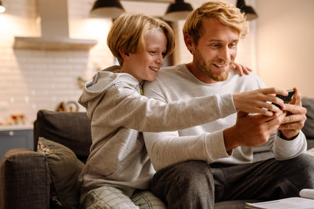 Ginger man using mobile phone while making fun with his son at homeの写真素材