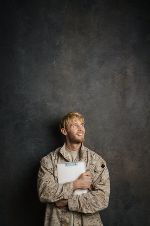 White military man wearing uniform smiling while posing with clipboard isolated over black backgroundの写真素材