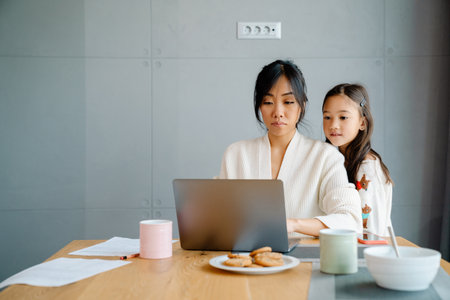 Asian woman working with laptop while her daughter doing homework at homeの写真素材