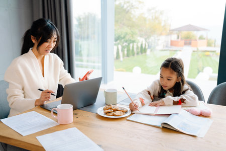 Asian woman working with laptop while her daughter doing homework at homeの写真素材