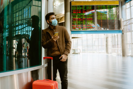 Indian man wearing face mask using mobile phone at train station indoorsの写真素材