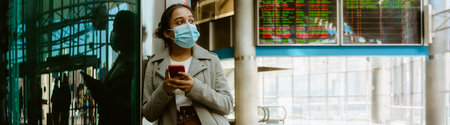 Indian woman wearing face mask using mobile phone at train station indoors