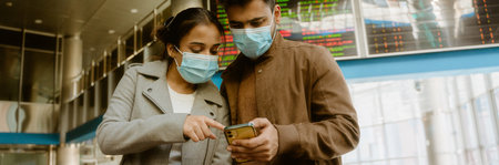 Indian couple wearing face masks using mobile phones at train station indoors