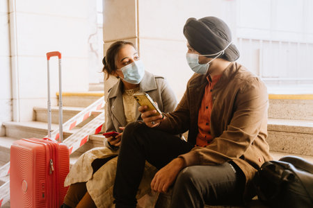 Indian couple wearing face masks talking and using mobile phones in airport indoorsの写真素材